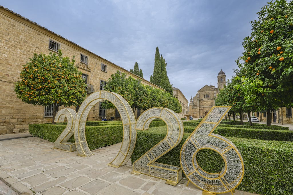 Scenic view of Úbeda, Spain featuring historic architecture and a large 2026 installation amidst orange trees and manicured hedges.