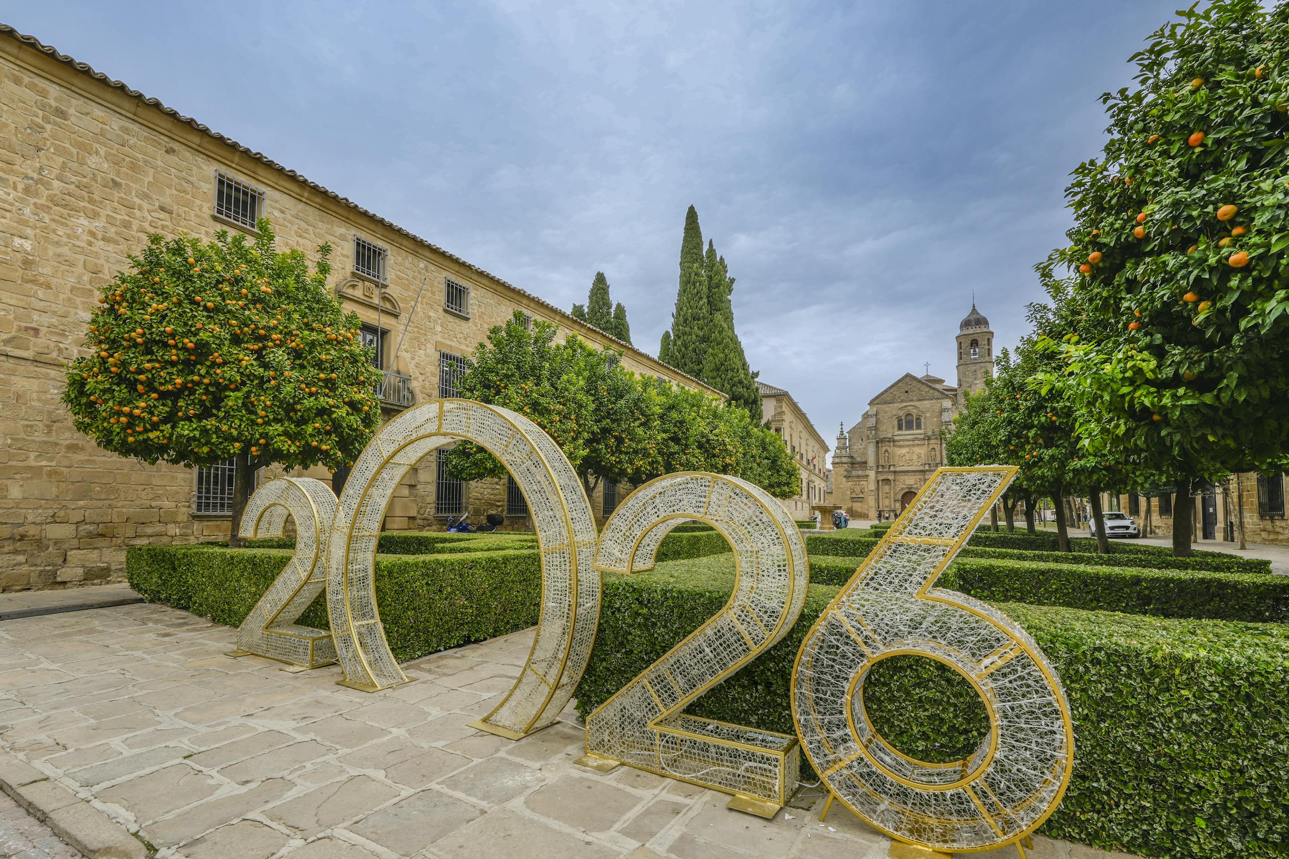 Scenic view of Úbeda, Spain featuring historic architecture and a large 2026 installation amidst orange trees and manicured hedges.